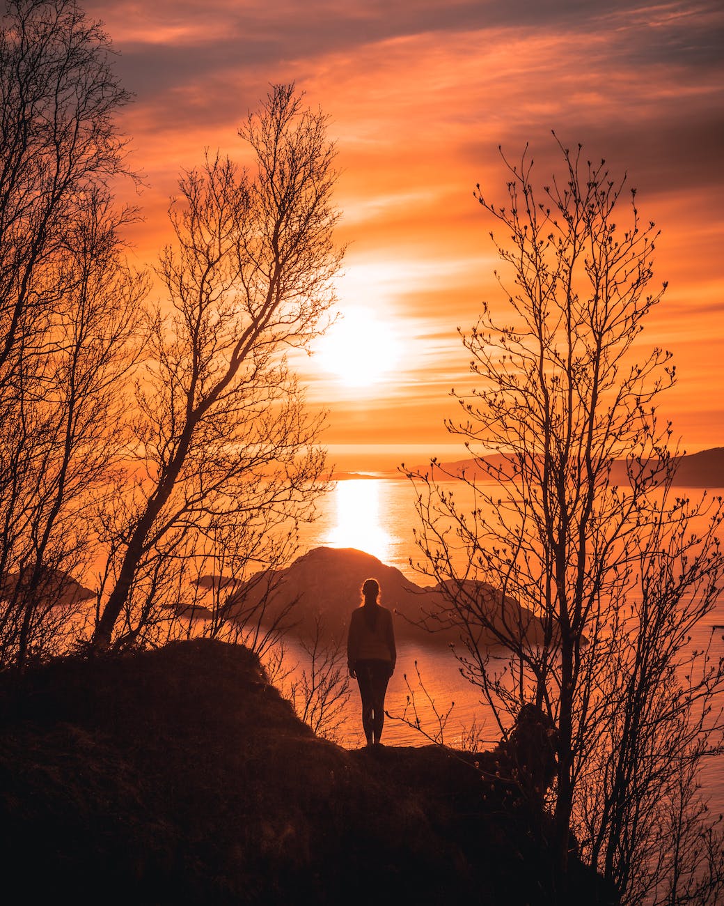 Woman standing on the edge of water staring at the sunset