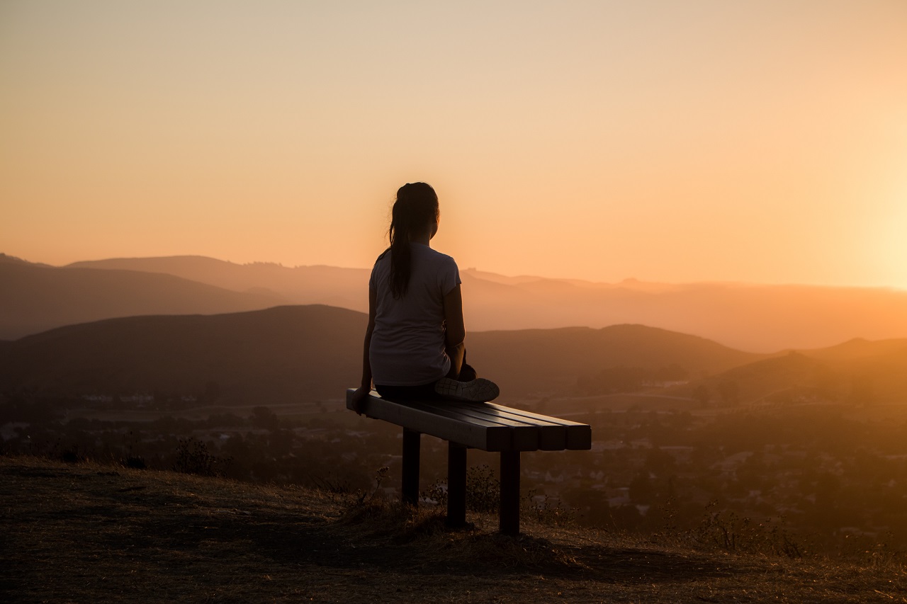 woman sitting on a bench watching the sunrise contemplating life